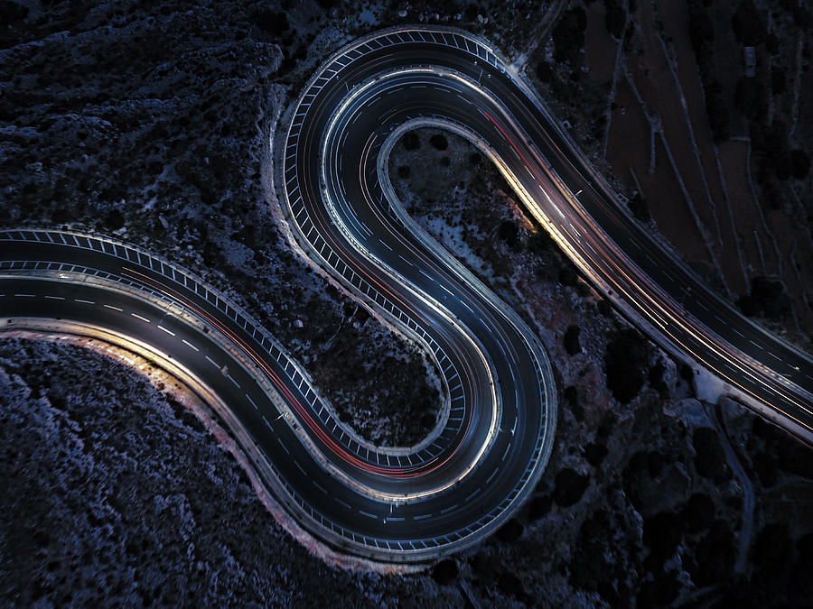 Aerial view of a winding road at night time. Cars light trails on an S-shaped rural road. Photograph by Felix Cesare