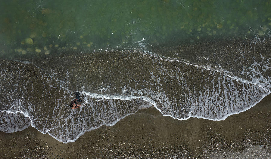 Aerial view of woman walking on the beach with ocean waves braking on a sandy beach. Photograph by Michalakis Ppalis