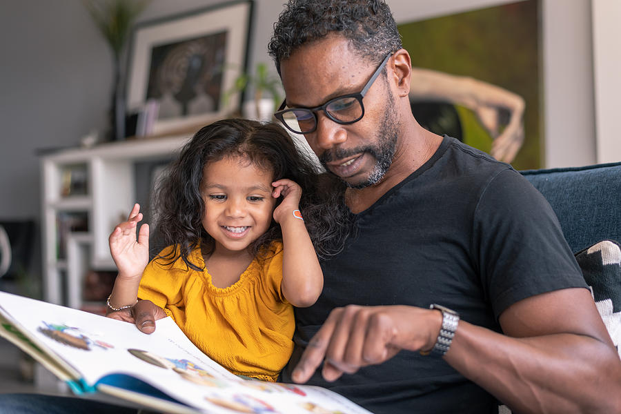 Affectionate father reading book with adorable mixed race daughter Photograph by Fly View Productions
