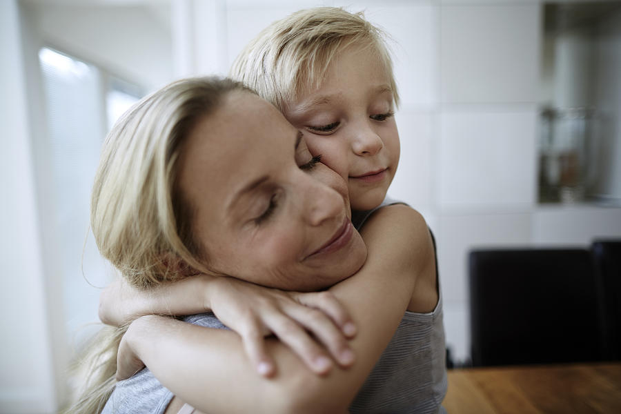 Affectionate mother and son with closed eyes hugging at home Photograph by Oliver Rossi