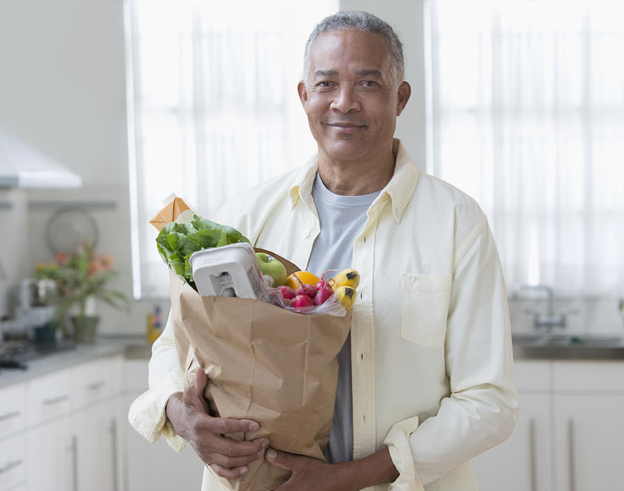 African American man carrying bag of groceries in kitchen Photograph by Jose Luis Pelaez Inc
