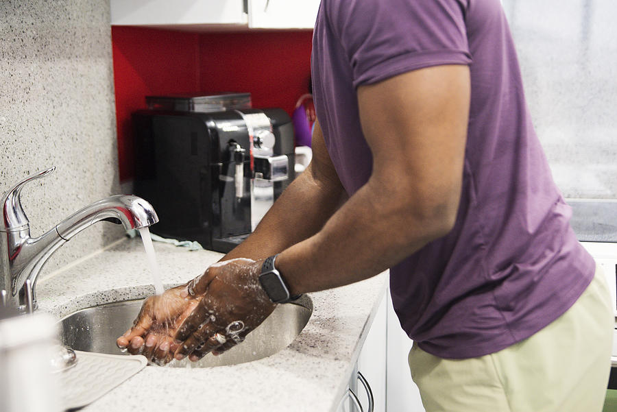 African-American man washing hands in kitchen sink. Photograph by Martinedoucet
