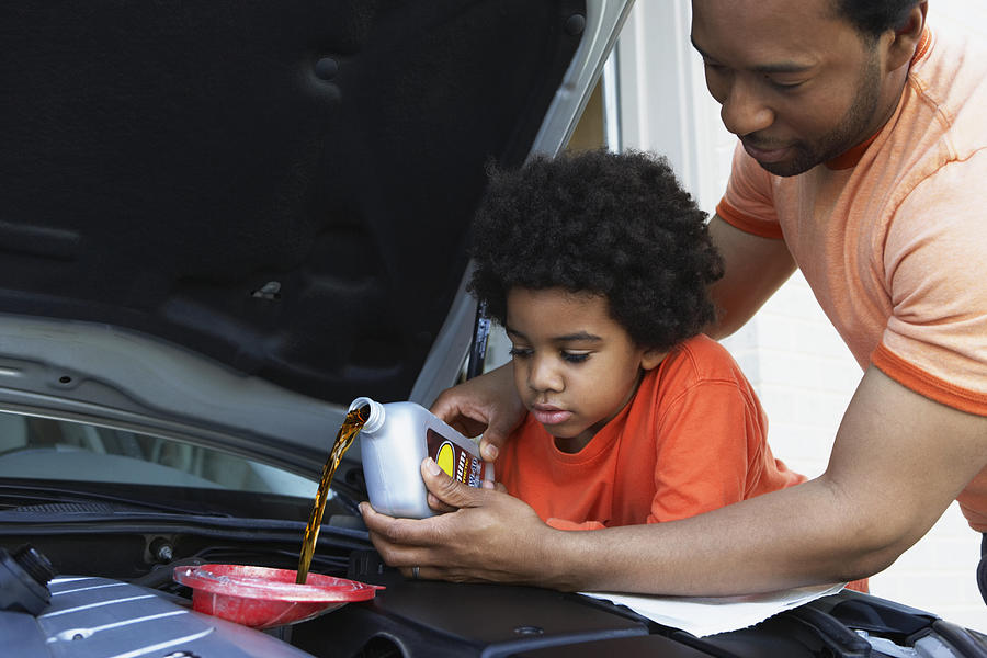 African father helping son pour oil into car engine Photograph by Jon Feingersh Photography Inc