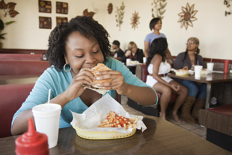 African woman eating hamburger in diner Photograph by Hill Street Studios