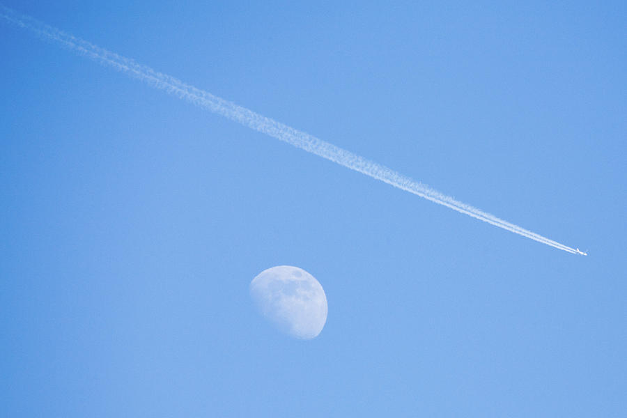 Aircraft flying over moon leaving vapour trail during the day, S Photograph by Ian Middleton