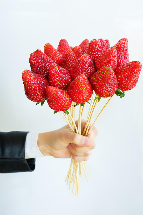 Alternative edible bouquet of berries in the hand of a man or woman, birthday, Valentines Day, holiday, close-up. Whole strawberry fruit on wooden skewers, on a white background. Selective focus. Photograph by Aleksandr Zubkov