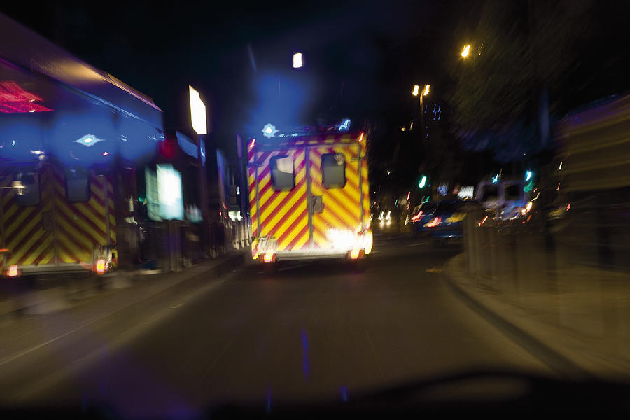 Ambulance driving on street at night Photograph by PhotoAlto/James Hardy