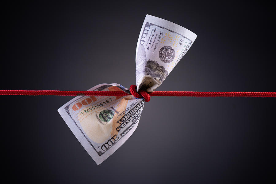 American dollar tied up in red rope knot on dark background with copy space. business finances, savings and bankruptcy concept. Photograph by Spukkato