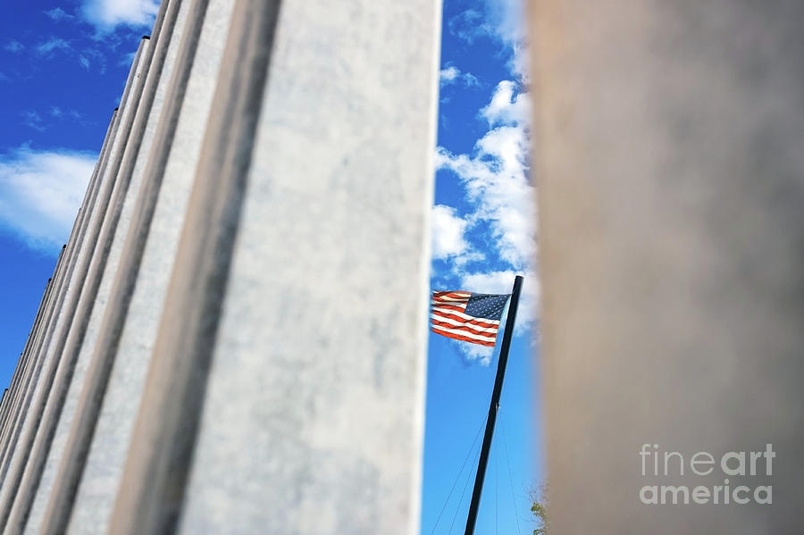 American flag waving across the border seen behind the bars of a barrier against immigrants. Photograph by Joaquin Corbalan