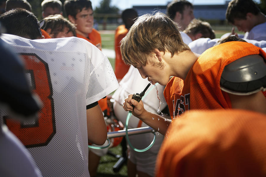 American football players including teenagers (15-17) in field, one drinking water Photograph by Darrin Klimek