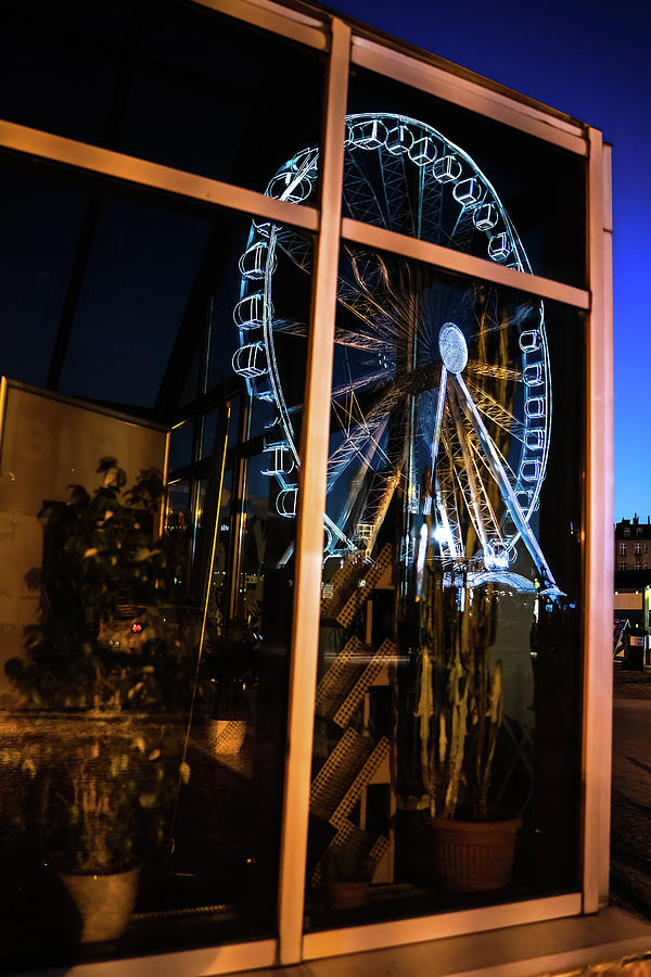 An abstract image containing reflection of a ferries wheel on a glass house with plants during night time located in Gdansk city of North Poland near Baltic sea Photograph by Arpan Bhatia