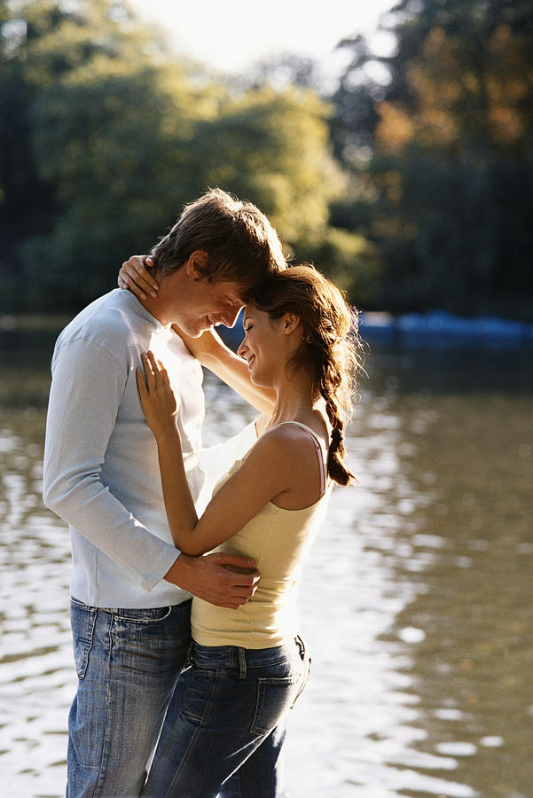 An Adoring Couple Stood Facing Each Other, Next to a Lake, in a Park Photograph by Digital Vision.