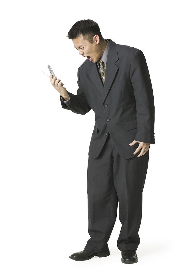 An Adult Asian Business Man In A Dark Suit Yells Angrily Into His Cell Phone Photograph by Photodisc