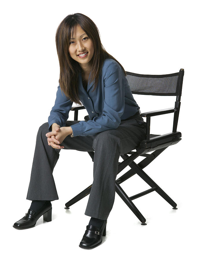 An Adult Asian Business Woman In Grey Pants And A Blue Shirt Sits In A Chair And Smiles Brightly Photograph by Photodisc