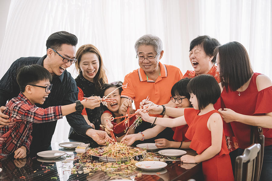 an asian chinese family celebrating chinese new years eve with traditional food Lou sang (raw fish dishes) during reunion dinner Photograph by Chee Gin Tan