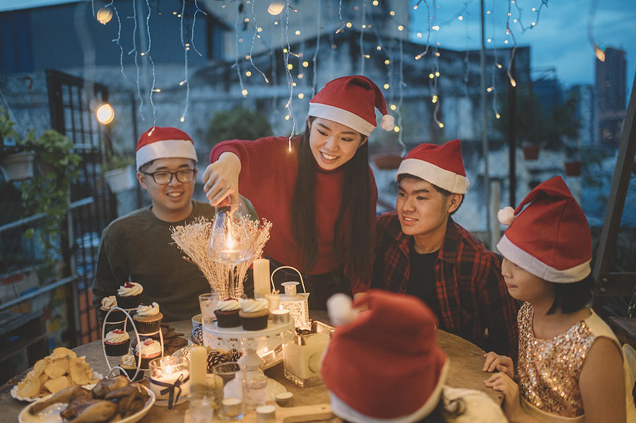An Asian Chinese Siblings And Friends Celebrating Christmas Dinner At Front Yard Of House Lighting Up Candle And Setting Up Table Photograph by Edwin Tan
