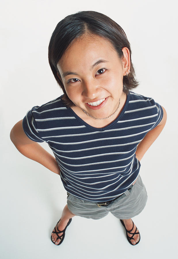 An Asian Young Woman Wearing Shorts And A Striped Teeshirt Smiles Sweetly Up At The Camera Photograph by Photodisc