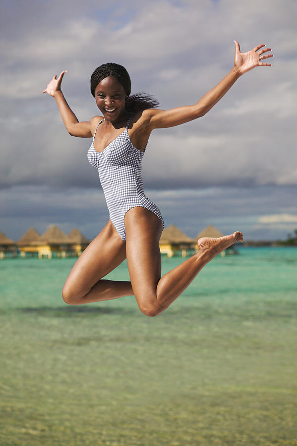 An Attractive African American Woman In A Swimsuit Jumps Up Into The Air Playfully At The Beach Photograph by Photodisc