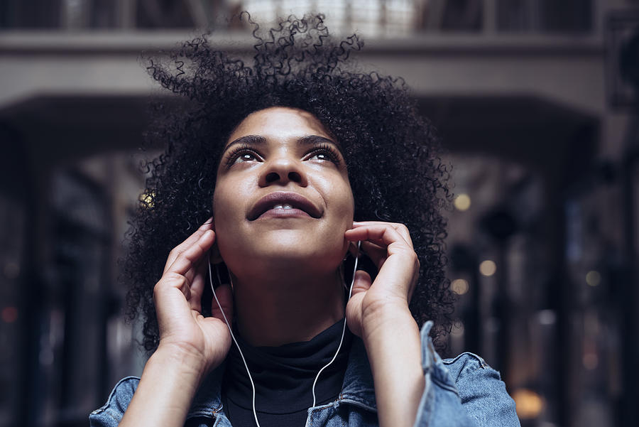 An attractive young woman with African American roots listens to music with headphones. She looks up dreamily and smiles slightly Photograph by Oliver Helbig