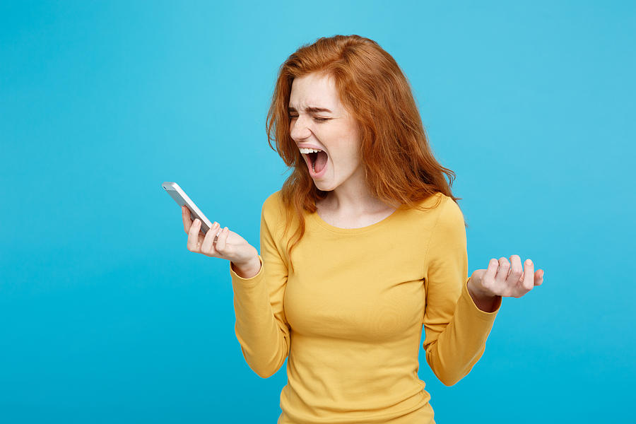 Angry Young Woman Screaming With Smart Phone Against Blue Background Photograph by Phongthorn Hiranlikhit / EyeEm