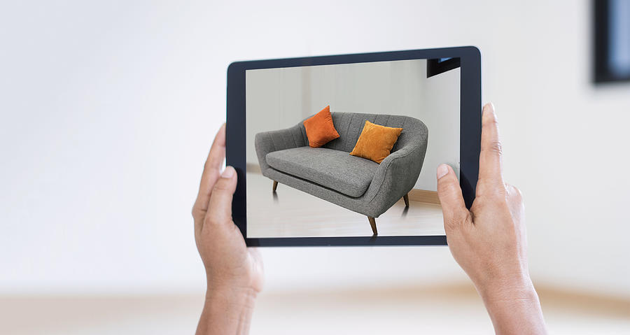 AR augmented reality. Hand holding digital tablet, AR application, simulate sofa furniture and and interior design real room background, modern technology. Photograph by Ipopba