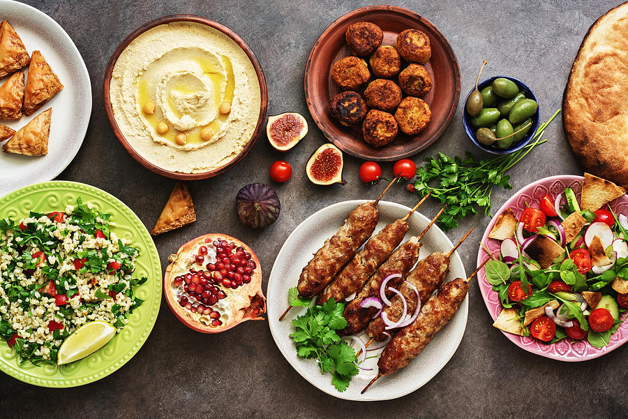 Arabic and Middle Eastern dinner table. Hummus, tabbouleh salad, Fattoush salad, pita, meat kebab, falafel, baklava, pomegranate. Set of Arabian dishes.Top view, flat lay Photograph by Yulia Gusterina