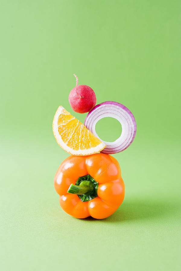 Arrangement of pepper, onion, orange and radish against green background Photograph by Image Source
