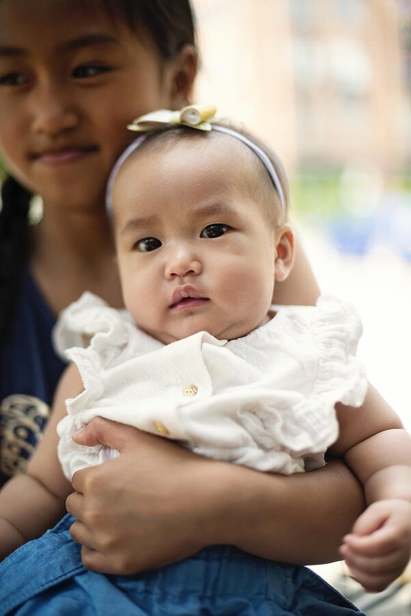Asian baby girl with big sister on restaurant terrace. Photograph by Martinedoucet