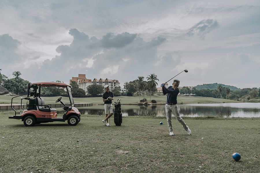 Asian Chinese Mature Man Golfer Is Preparing To Teeing Off At Golf Course While His Son Is Observing Photograph by Patrick Chu