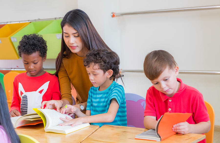 Asian female teacher teaching diversity kids reading book in classroom,Kindergarten pre school concept. Photograph by Weedezign