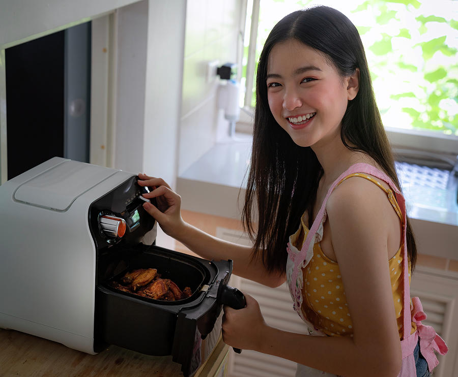 Asian girl cooking a fried chicken by Air Fryer machine Photograph by Anek Suwannaphoom
