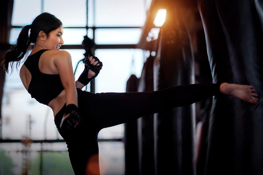 Asian girl kick a sand bag in kickboxing gym Photograph by Anek Suwannaphoom