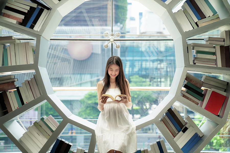 Asian girl reading on a bookshelf in a library Photograph by Anek Suwannaphoom