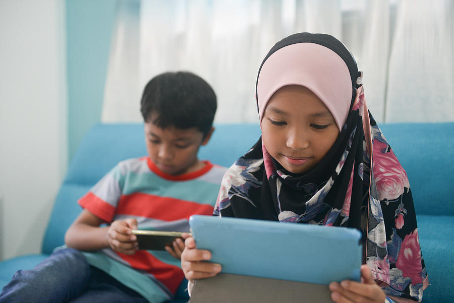 Asian Malay Muslim Children uses smart phone & tablet at home in Malaysia Photograph by Zuraisham