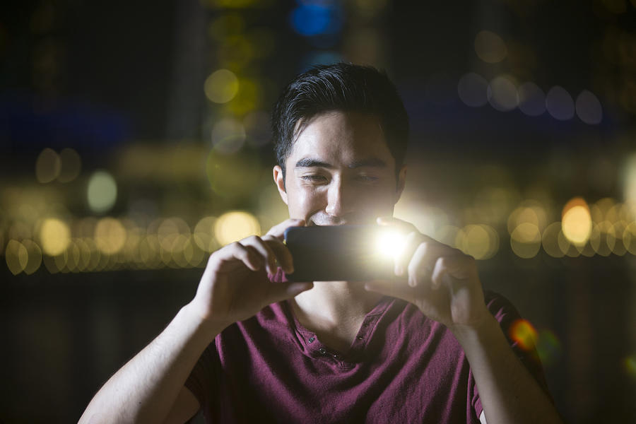 Asian man using his smart phone to take a photo at night. Photograph by Jenner Images