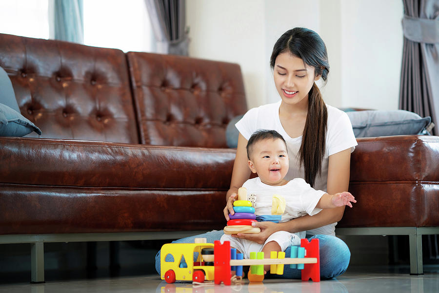 Asian mother and baby play togather with wooded toy on sofa Photograph by Anek Suwannaphoom