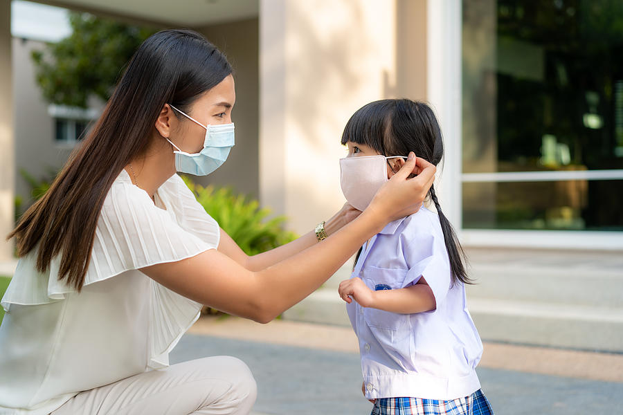 Asian mother help her daughter wearing medical mask for protection Covid-19 or coronavirus outbreak in village park to prepare go to school when back to school order. Photograph by Ake1150sb