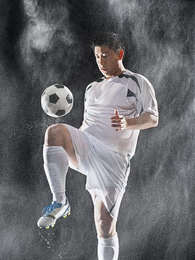 Asian soccer player kicking ball in rain Photograph by Erik Isakson