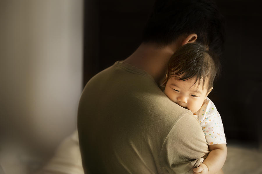 Asian toddler carried by father in moody bedroom background. Photograph by Twomeows