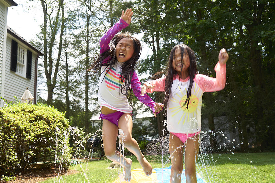 Asian Twin girls playing on slip and slide Photograph by Chris Stein