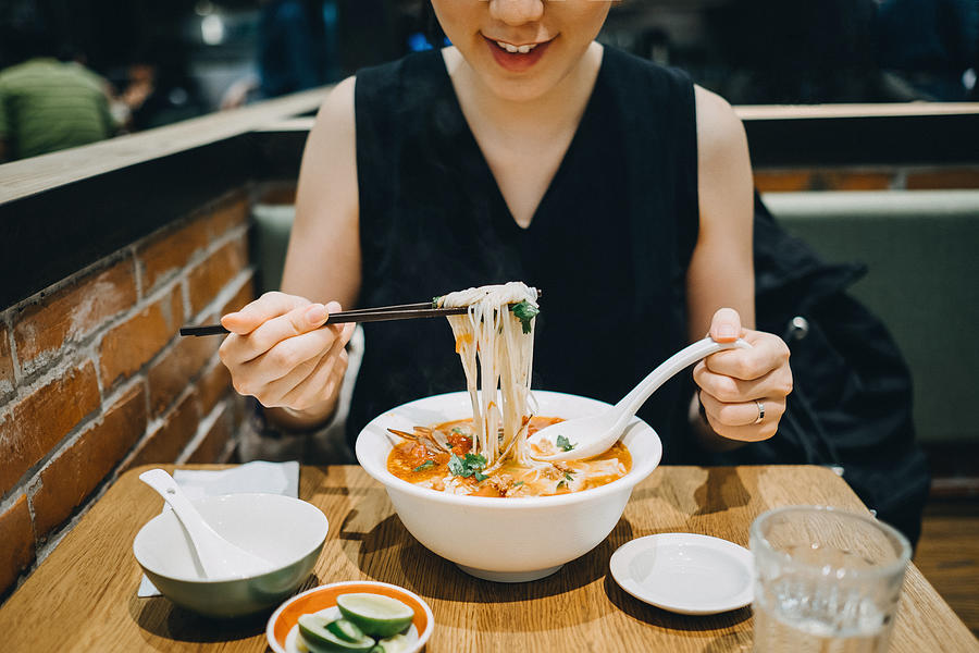 Asian woman eating soup noodles joyfully in restaurant Photograph by D3sign