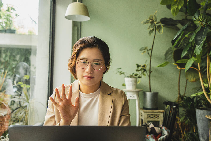 Asian woman waving at a laptop at a cafe Photograph by Kilito Chan