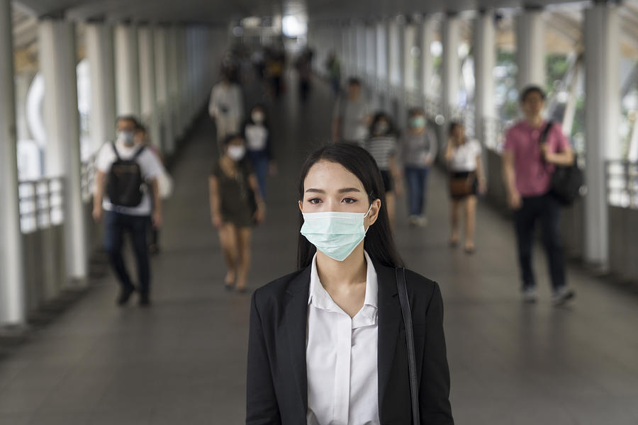 Asian woman with protective face mask in the urban bridge in city against crowd of people Photograph by Thana Prasongsin
