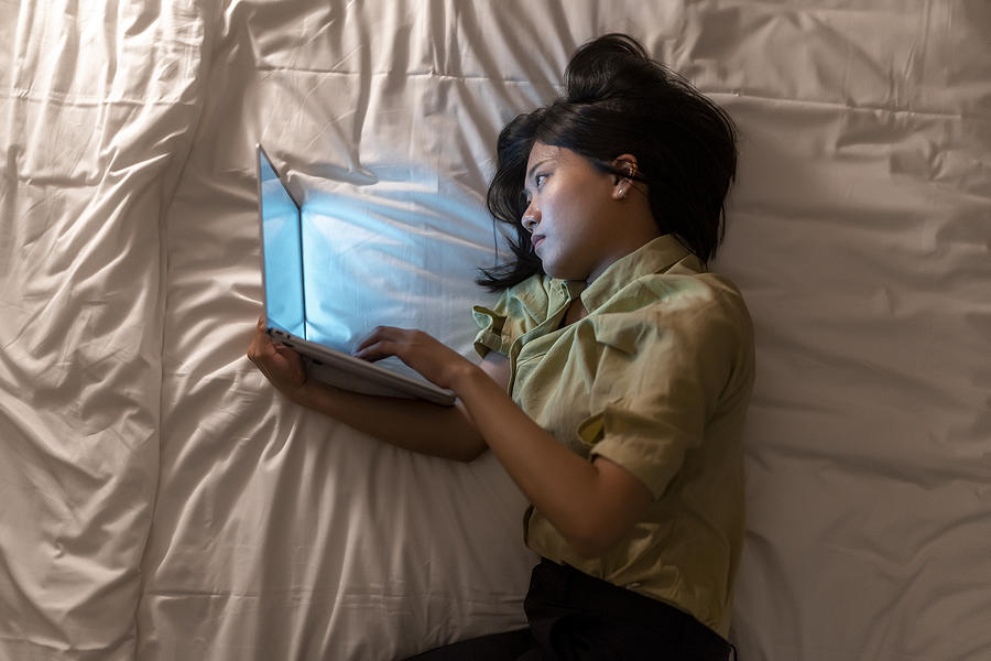 Asian woman working late at bedroom Photograph by Sellwell