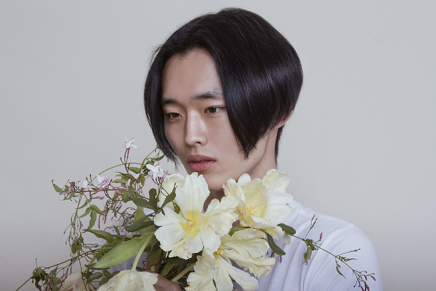 Asian young adult male holding and smelling bouquet of flowers Photograph by Rachel Thalia Fisher