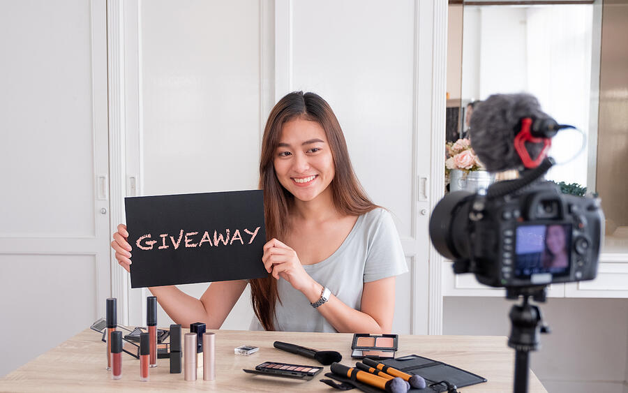 Asian young female blogger giveaway gift to fan following channel while recording vlog video with makeup cosmetic at home online influencer on social media concept.live streaming viral. Photograph by Weedezign