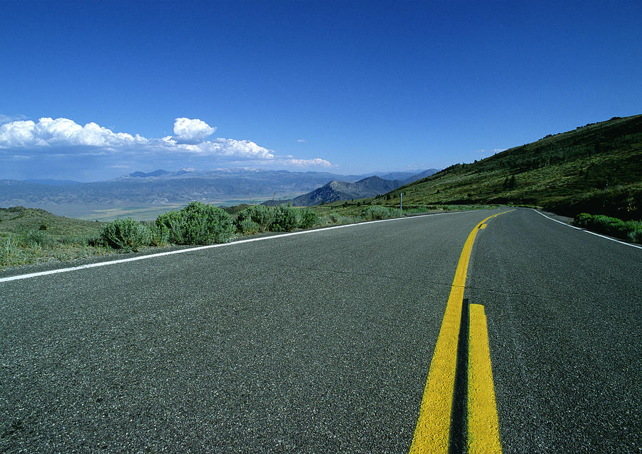Asphalt road with yellow lines overlooking mountainous region. Photograph by James Hardy