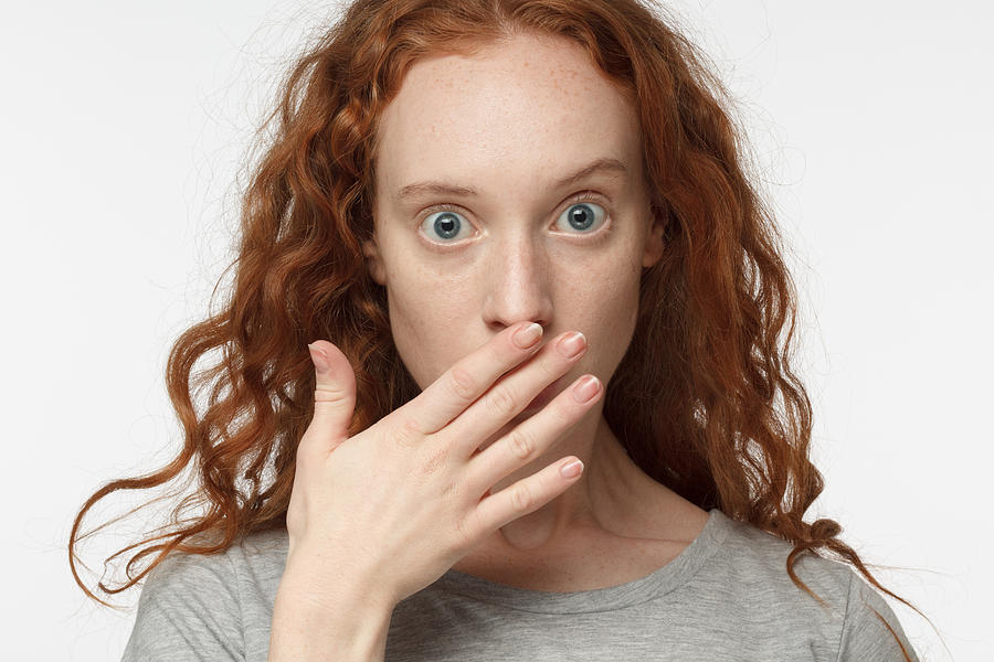 Astonished bug-eyed curly redhead girl covering her mouth with one hand, looking shocked. Surprised, embarrassed and confused female showing omg emotion Photograph by Damir Khabirov