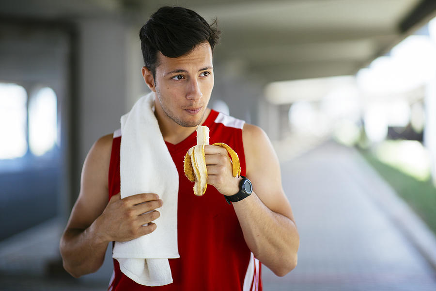 Athletic man eating banana after workout outdoors Photograph by Ciricvelibor