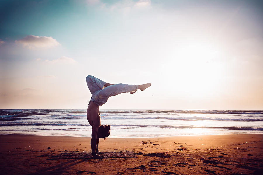 Athletic man practising yoga on the beach at sunset Photograph by Wundervisuals